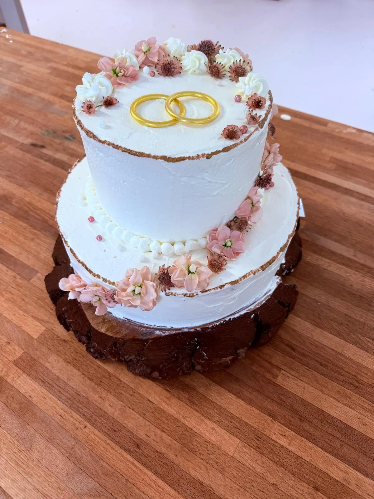 Zweistöckige weiße Hochzeitstorte mit Goldringen und rosa Blüten