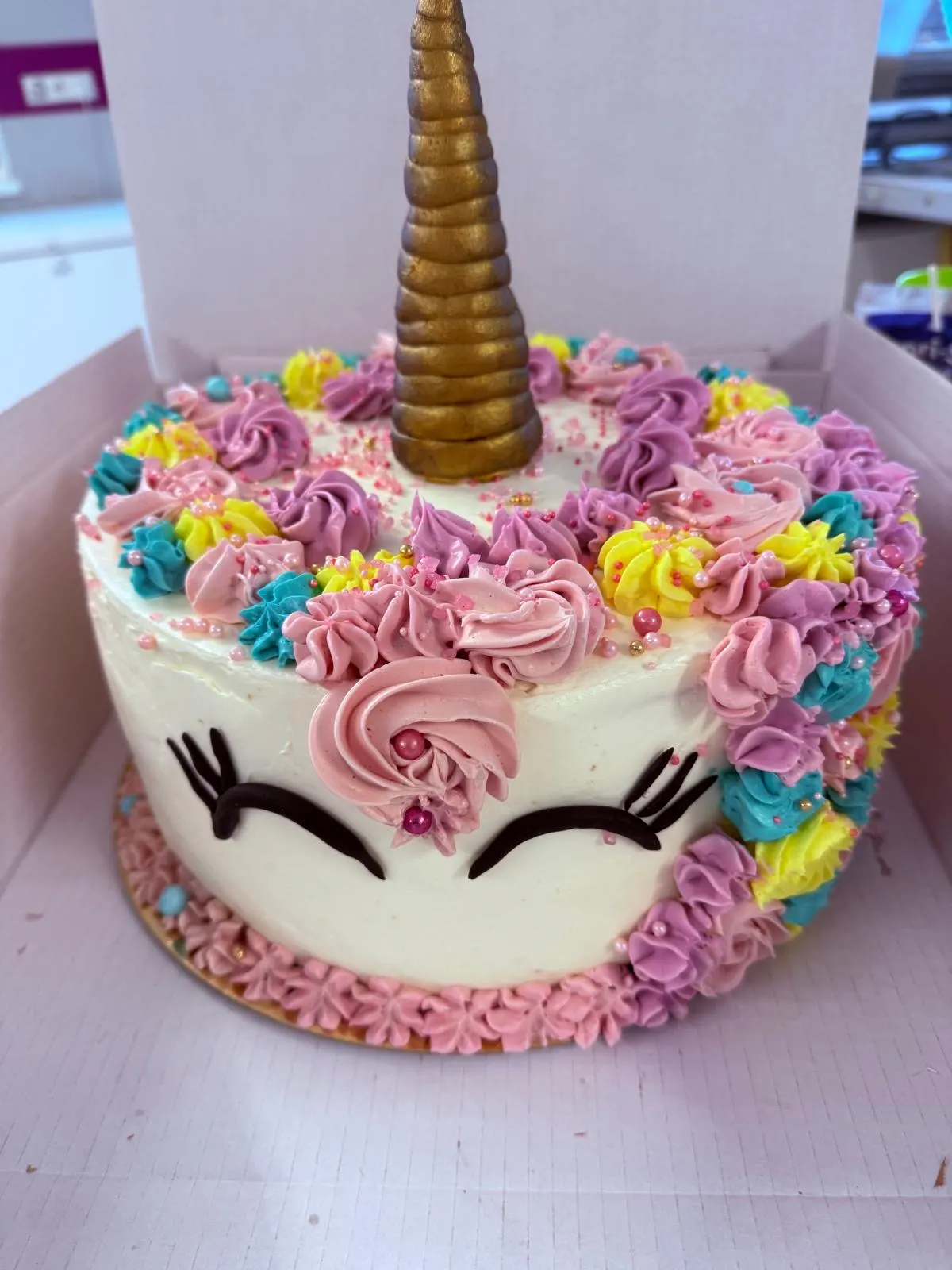 Einhorntorte mit goldenem Horn und bunten Sahnerosetten