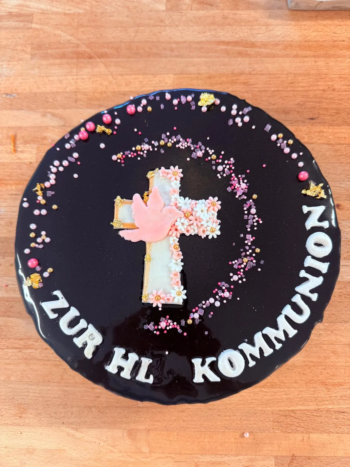 Kommuniontorte mit dunkler Glasur, Blütenkreuz, rosa Taube und Zuckerperlen